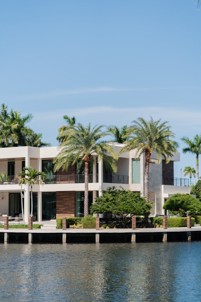 Modern luxury villa by the waterfront surrounded by palm trees, under a clear blue sky.